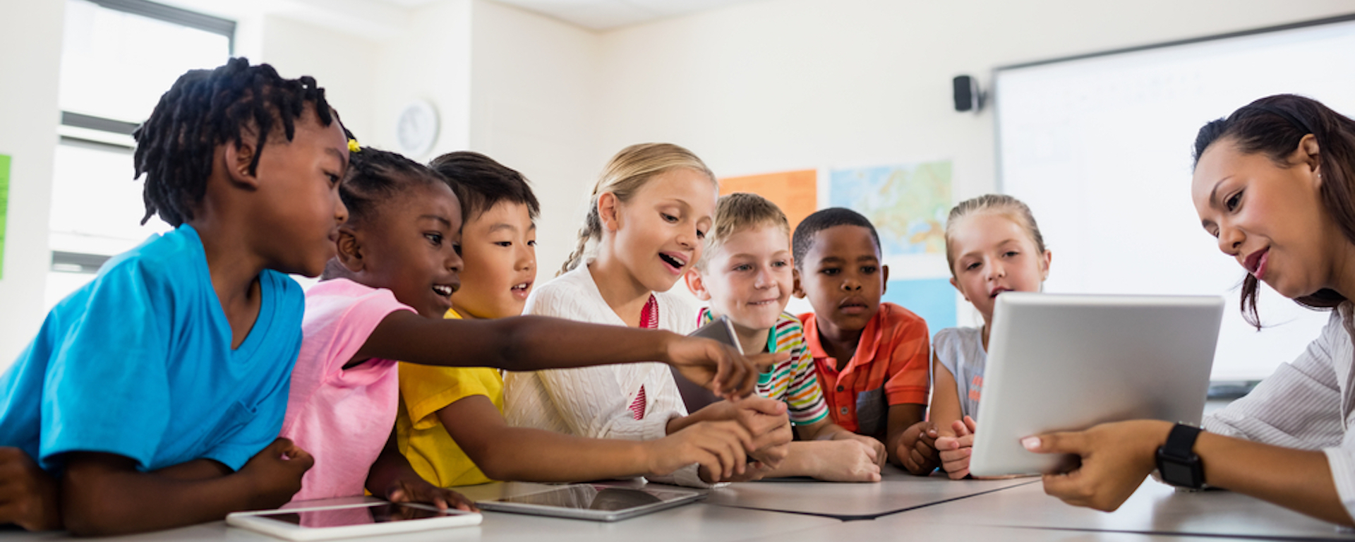  A group of students sit around a table with a teacher using tablets in the classroom.