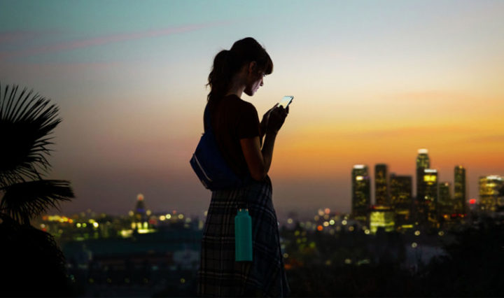 Woman using a 5G-enabled smartphone outside a connected cityscape