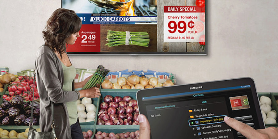 A customer shops for produce in front of digital signage displaying prices and specials